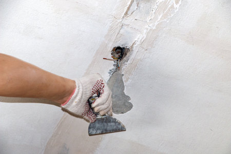mans hand in a cloth glove with a spatula and putty, applies mastic to wall, ceiling to level surface. process of applying mastic with a spatula to surface for interior design of the room.の写真素材