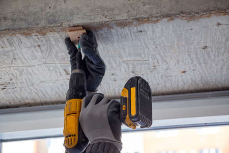 male hands of a construction worker tighten and fix screws and self-tapping screw with an electric...