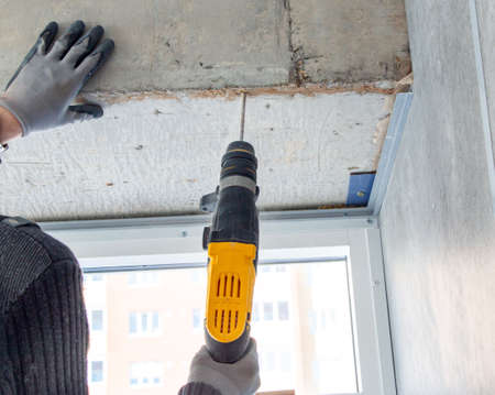male hands of a construction worker drills a hole in concrete with a hand drill. the process of drilling holes in concrete beams and crossbar for various fastenings using an impact drill.の写真素材