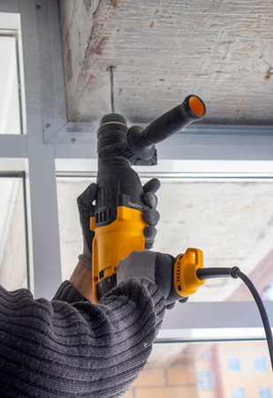 male hands of a construction worker drills a hole in concrete with a hand drill. the process of drilling holes in concrete beams and crossbar for various fastenings using an impact drill.の写真素材