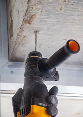male hands of a construction worker drills a hole in concrete with a hand drill. the process of drilling holes in concrete beams and crossbar for various fastenings using an impact drill.の写真素材