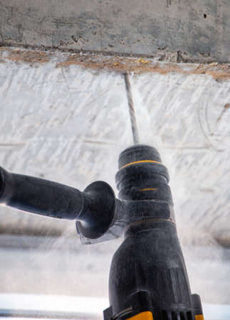 male hands of a construction worker drills a hole in concrete with a hand drill. the process of drilling holes in concrete beams and crossbar for various fastenings using an impact drill.の写真素材