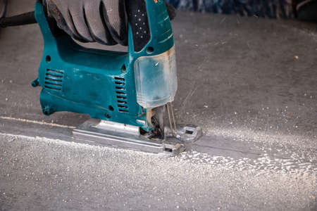 male hands of a construction worker sawing and cutting parts with an electric hand jigsaw from a...