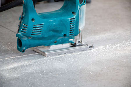 male hands of a construction worker sawing and cutting parts with an electric hand jigsaw from a panel. the process of cutting a building board for interior decoration with an electric jigsawの写真素材
