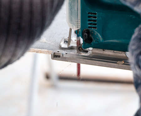 male hands of a construction worker sawing and cutting parts with an electric hand jigsaw from a panel. the process of cutting a building board for interior decoration with an electric jigsawの写真素材