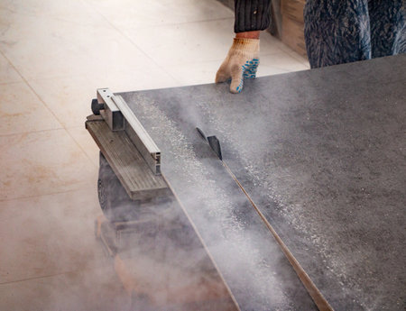 male hands of a construction worker sawing and cutting parts of an electric miter saw from a wooden board. wood board cutting process with blade rotation and dusty cloud electric miter sawの写真素材