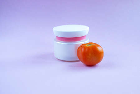 Cream and mask for skin care in a white jar and tube with a dispenser near bright juicy tomatoes....