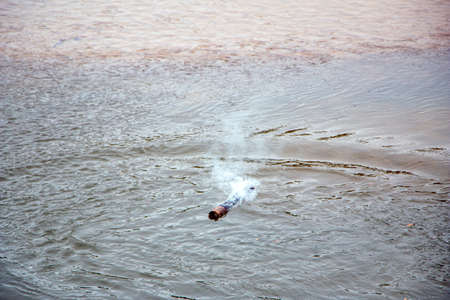 Wooden pine is crawled after a fire, covered with coal and sparks, and sails on the surface of the river water, by flow, creating waves and clouds of smoke from burning.の写真素材