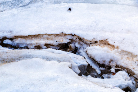 Cracks on thick ice on the surface of a frozen river in the winter season, powdered by snow and...