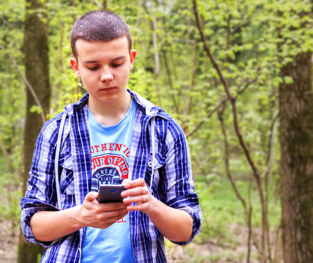 Young man stands in the woods, thinks about something and works on the phoneの写真素材