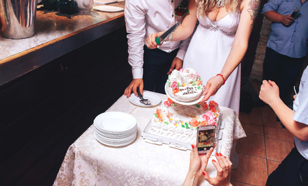 Happy wedding couple handsome groom and blonde bride carving delicious wedding cake