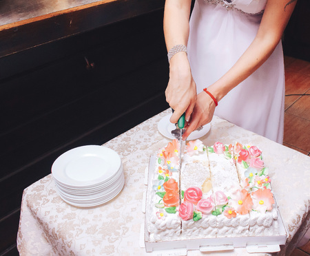 Happy wedding couple handsome groom and blonde bride carving delicious wedding cake
