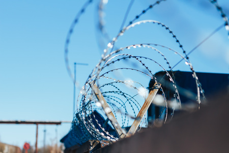 Barbed wire on top of the concrete fence with blue sky with clouds closeup