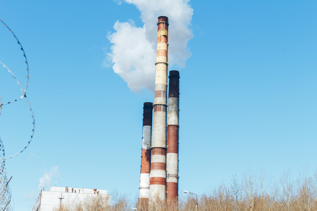 Large pipes of the heat station smoke against the sky with cloudsの写真素材