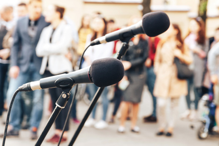 Two microphones stand in the street in front of a group of peopleの写真素材