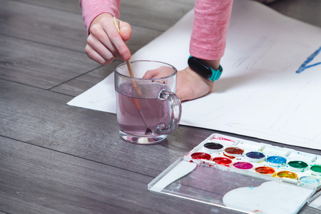 The hand of a young girl dunks into the water to paint multicolored letters.の写真素材