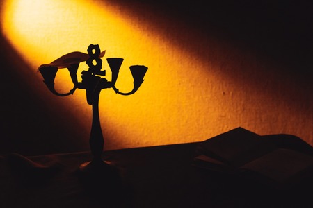 An old candlestick stands in the dark next to a ray of light.