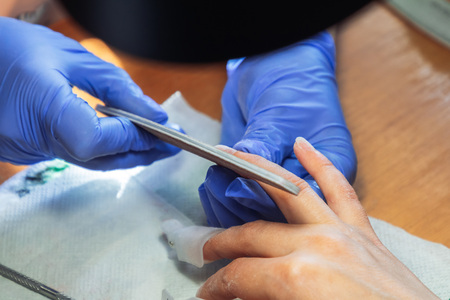 A manicurist handles a woman s finger with a nail file. Other fingers of the hand are in manicure...