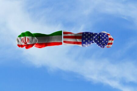 The concept of two hands of mature men painted in the colors of the flags of Iran and the United States against a blue sky.の写真素材
