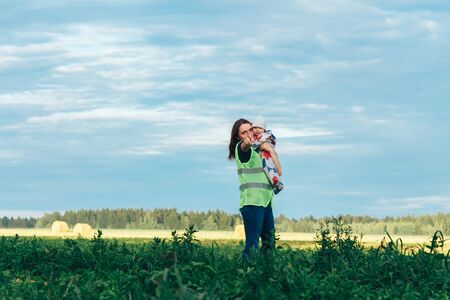 July 6-7, 2019 Village Petrevichi Minsk region Belarus Beetle trail 12 Midsummer The girl in the signal jacket stands with the child on the background of a beautiful view of natureのeditorial素材