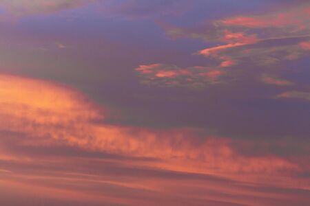 Colorful dramatic sky at sunset with layered rain clouds of purple and gold color
