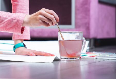 Young girl rinses a brush for painting in a mug with waterの写真素材
