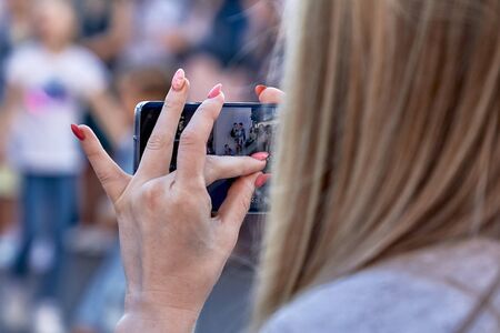 Woman taking a photo of street people with smartphone in cityの写真素材