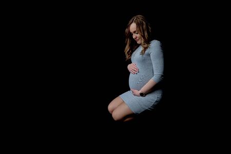 Pregnant woman crouched on a black backgroundの写真素材