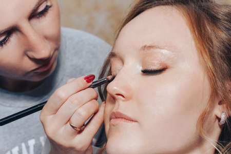 August 10, 2019 Minsk Belarus Close-up woman hairdresser does girl's eye makeup at home. Private practice at homeのeditorial素材