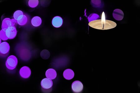 The concept of prayer and hope.The concept of prayer and hope.Flame of a burning candle at night with abstract round bokeh purple background of Christmas lights.の写真素材