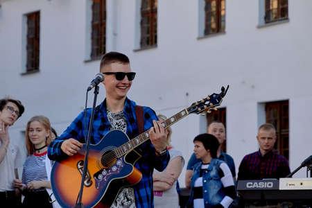 June 1, 2019 Minsk Belarus A young happy musician with glasses plays the guitar standing on the streetのeditorial素材