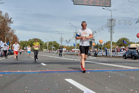 September 15, 2019 Minsk Belarus An elderly man crosses the finish line of a marathon by checking his heart rate on his smartwatchのeditorial素材