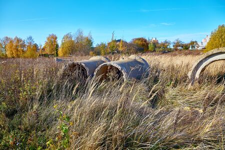 Big old concrete pipes lie in the grass under a blue skyの写真素材