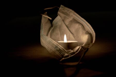 A candle flame burns in a protective medical mask against coronavirus on a dark backgroundの写真素材