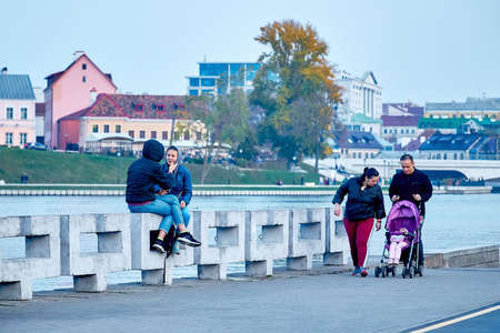 October 19, 2019 Minsk Belarus Young family walking along the river bank at the time when the two girls are sitting on concrete slabsのeditorial素材