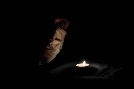 Profile of a masked person, the concept of a viral infection.A burning candle in the dark. Theme of the corona virus outbreak.の写真素材