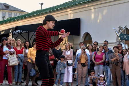 May 25, 2019 Minsk Belarus Girl dressed as a clown shows focus with a red ball in the city. People stand nearby in blur.のeditorial素材