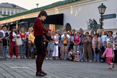 May 25, 2019 Minsk Belarus Girl dressed as a clown shows performance with a red ball at the street. People stand nearby in blurのeditorial素材