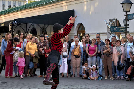 May 25, 2019 Minsk Belarus Girl dressed as a clown shows focus with a red ball in the evening city. People stand nearby in blur.のeditorial素材