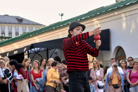 May 25, 2019 Minsk Belarus Girl dressed as a clown shows focus with a red ball in the city. People stand nearby in blur.のeditorial素材
