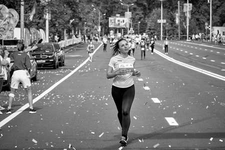 September 15, 2019 Minsk Belarus In the black-and-white image, a woman runs ahead of the participants of the half marathon in Minsk.のeditorial素材