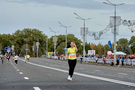 September 15, 2019 Minsk Belarus There a happy young woman with a smartphone in her raised hand takes a selfie while running a marathonのeditorial素材