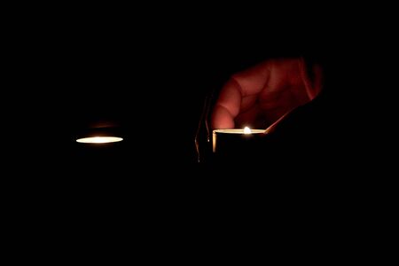 There are two candles burning and a human hand is seen holding a burning candleの写真素材