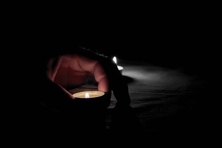 There is a human hand putting a burning candle on the table on memorial dayの写真素材