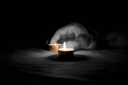 Here is a human hand placing a burning candle on a table on a black backgroundの写真素材