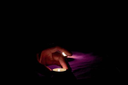 A man puts a burning candle on a purple table next to a burning candle in the darkの写真素材