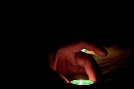 A human hand places a burning green candle on the table next to a burning candle in the darkの写真素材