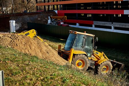 Yellow loader backhoe digs under the road during road construction works.の写真素材