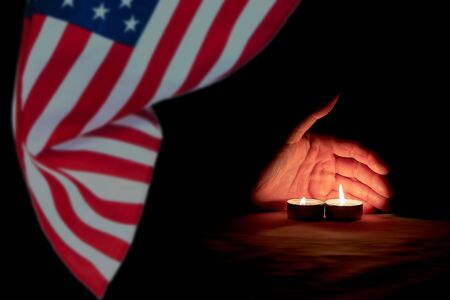 A human hand is illuminated by burning candles against the background of the US flag on memorial dayの写真素材