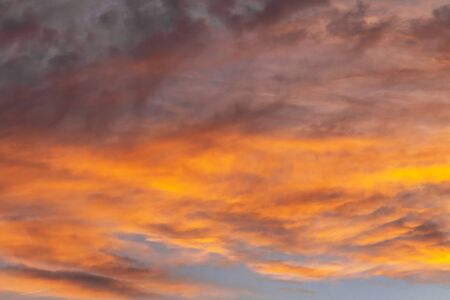 Colorful dramatic sky at sunset with layered rain clouds of bright blue and orange. A beautiful picture can be associated with depressionの写真素材